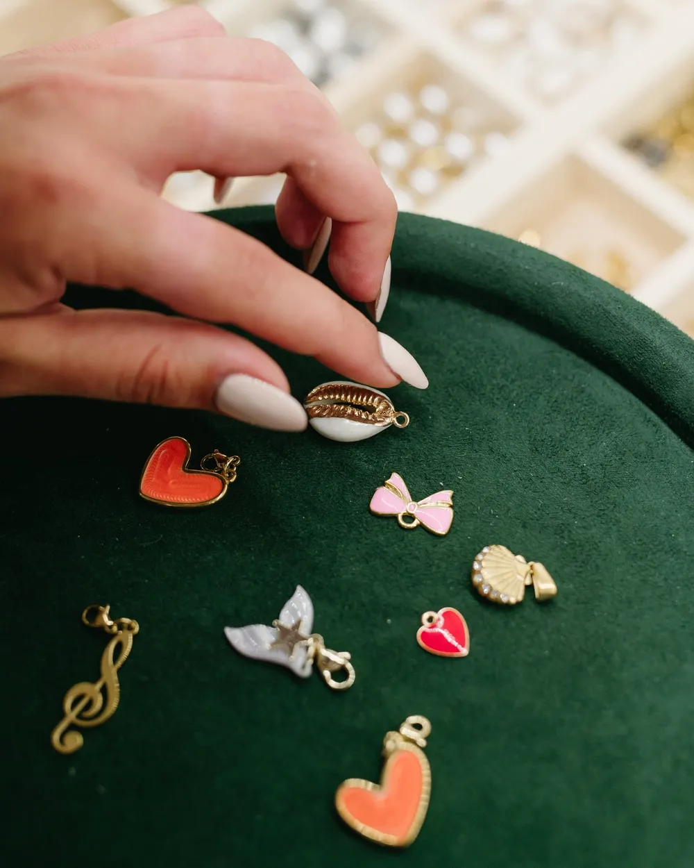 A hand placing a shell charm on green velvet next to hearts, a bow and a treble clef